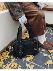 Detail of a large black Boston tote bag with metal rivets and straps in an autumn street setting