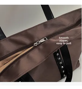 Detail view of smooth metal zipper and brown textured fabric on studded tote bag
