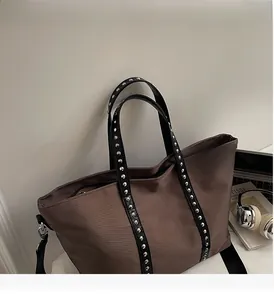 Detail of chocolate brown large tote bag featuring silver studs on black leather straps