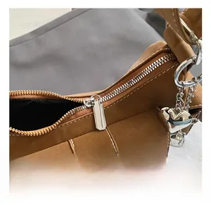 Detail of brown suede baguette bag featuring white stitching and silver heart charm
