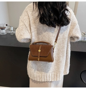 Detail of brown matte leather handbag with gold circular buckle in a cafe setting