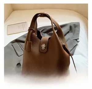 Detail of brown lychee grain leather bucket bag with gold metal buckle on a grey blazer