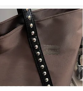 Close-up of brown textured tote bag with silver cone rivets on black leather strap