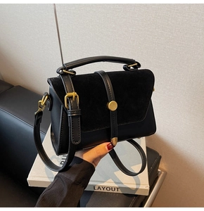 Detailed close-up of a matte black handbag with suede flap and gold vintage hardware