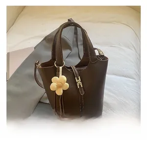 Detail of brown litchi pattern leather bucket bag with daisy charm on bed