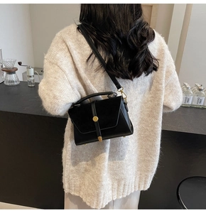 Detail of black crossbody bag featuring matte leather flap and gold hardware accents