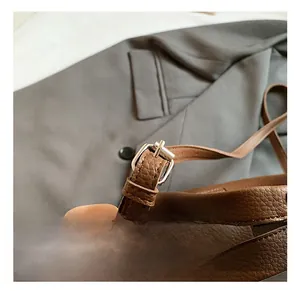 Detail view of silver metal buckle and litchi grain leather strap on brown bucket bag