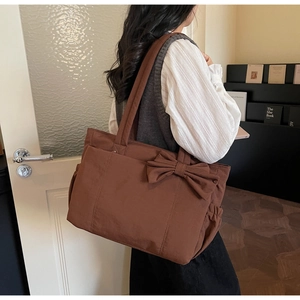 Grand sac cabas marron avec nœud décoratif, porté à l'épaule par une femme élégante