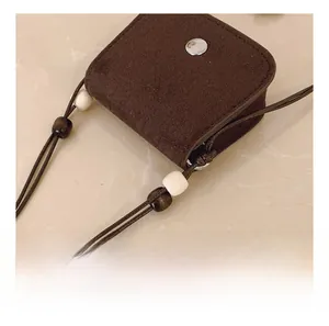 Detailed close-up of brown suede mini pouch with silver snap and decorative neck strap beads