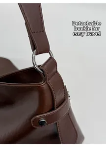Détail de la boucle métallique amovible sur un sac à bandoulière en cuir marron foncé