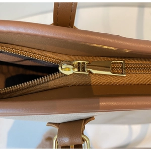 Detailed close-up of premium light gold metal zipper and stitching on brown leather bag