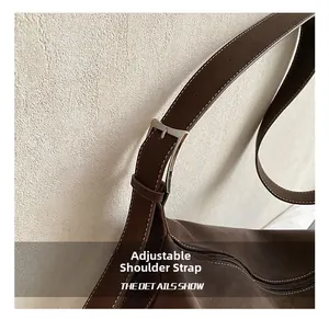 Detail of adjustable shoulder strap with silver buckle and white stitching on brown suede tote