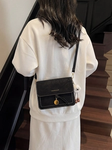 Detail of black crossbody bag with white stitching and plush eye charm on leather strap