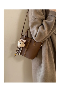 Detail of dark brown lychee textured handbag with cute teddy bear charm accessory