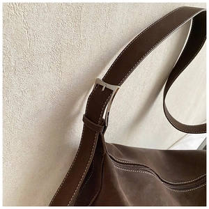 Detail of silver metal buckle and contrast white stitching on dark brown suede tote bag