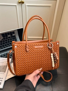 Brown pleated bucket bag with beaded charm and shoulder strap in an office setting
