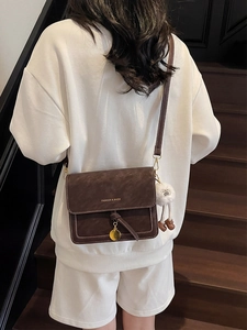 Detail of vintage brown crossbody bag with white stitching and white plush doll charm