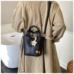 Detail of black lychee leather bucket bag with flower charm on a trench coat model