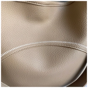 Close-up of litchi grain leather texture with white zigzag stitching on khaki bucket bag