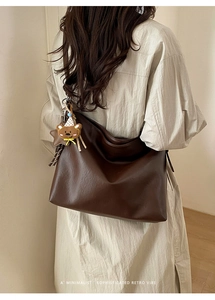 Détail d'un grand sac cabas en cuir marron foncé avec pendentif ours sur un modèle en robe