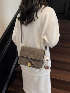 Deep grey matte crossbody bag with gold pendant and fluffy charm on a female model