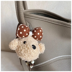 Detail of plush bear bag charm with polka dot bow on a gray textured leather handbag
