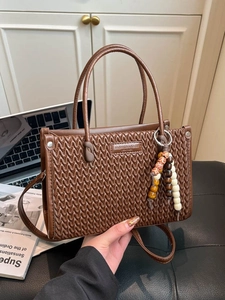 Brown woven bucket bag with beaded charm accessory shown in a modern lifestyle setting