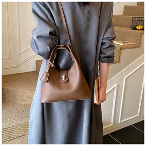 Close-up of brown litchi pattern leather bucket bag with metal lock worn by a model