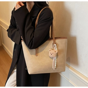 Detail of oat-colored tote bag with brown leather handles and plush bear charm