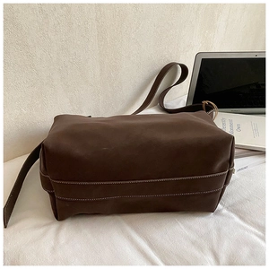 Deep brown bucket bag with contrast white stitching shown on a minimalist white desk