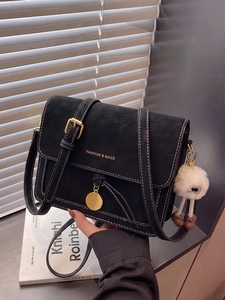 Detail of black matte shoulder bag with white stitching and plush ball charm