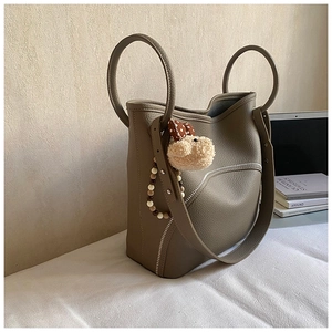 Detail of khaki leather bucket bag with circular handle, wide strap and plush pendant