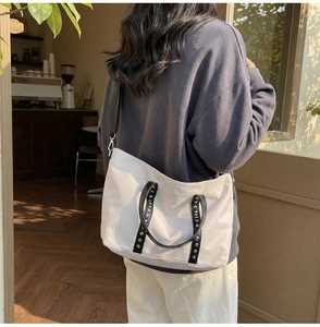 Détail du sac fourre-tout crème avec poignées à rivets noirs et bandoulière réglable