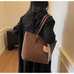 Detail of vintage brown tote bag with metal strap buckle and cute plush bear charm