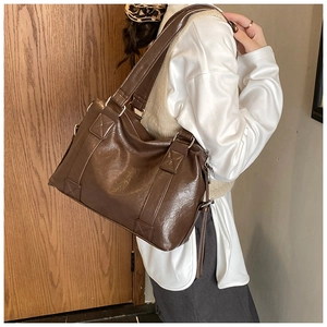 Detail of dark brown leather tote bag with decorative cross-stitching on model