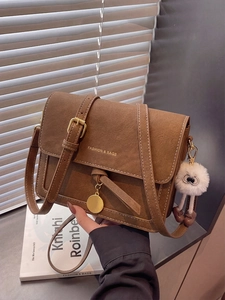 Detail of brown vintage crossbody bag featuring matte texture and plush ball charm