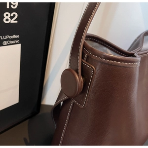 Close-up of deep brown leather bucket bag with contrast white stitching and round buckle