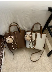Detail view of lychee pattern leather bucket bags in dark brown and beige with cute charms