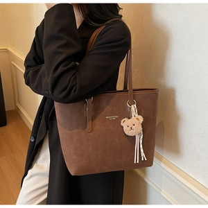 Detail of dark brown leather tote bag with teddy bear charm and striped ribbon accent