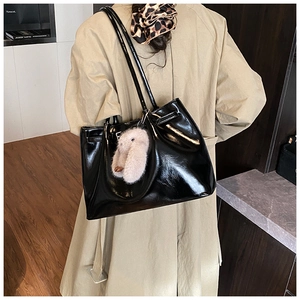 Détail d'un sac cabas en cuir verni noir brillant avec un pendentif lapin rose