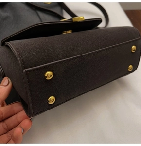 Detail of dark brown matte leather bag featuring gold protective feet and smooth texture