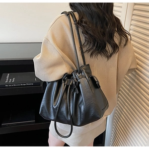 Detail of a black leather drawstring bucket bag with star charm worn by a model
