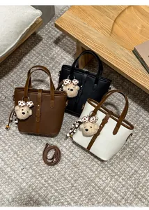 Three leather bucket bags in brown, black, and bicolor with cute teddy bear pendants