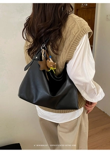 Détail d'un sac cabas noir avec pendentifs ours et étoile porté sur un pull tricoté