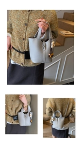 Detailed views of grey lychee leather bucket bag with sunflower pendant on indoor stairs
