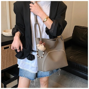 Detail of grey leather bucket bag with silver zipper and plush bear charm on model