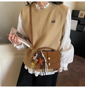 Close-up of retro brown satchel with plush bear charm and striped tassel accessories