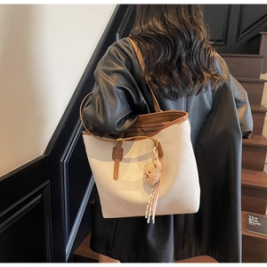 Detail of a beige tote bag with brown straps and a plush bear charm on a model