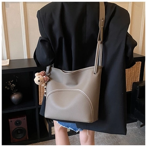 Detail of taupe lychee leather bucket bag featuring a front zipper pocket and cute bear charm