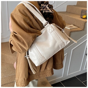 Close-up of cream faux leather tote featuring cross-stitch strap detail and silver zipper